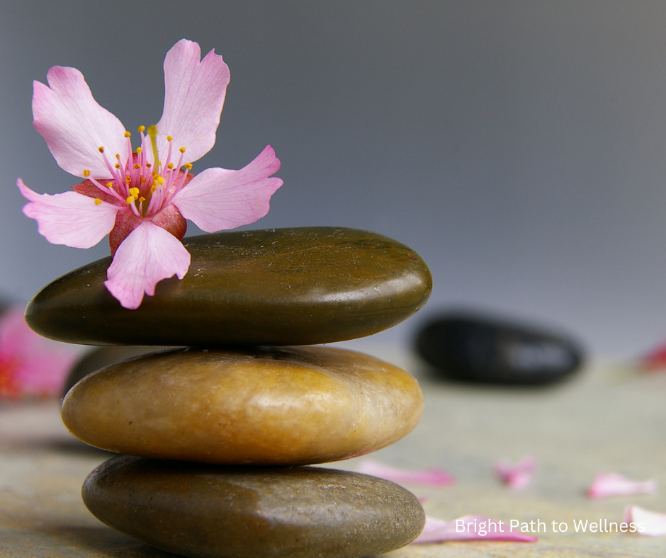 Three stones, one on top of the other, and a pink flower on top.