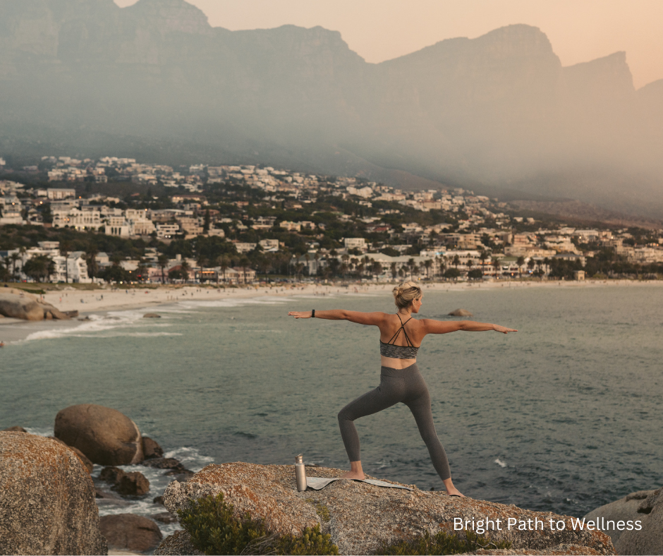 A woman exercising on top of a mountain overlooking a bay.