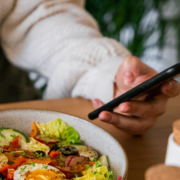a person looking at the cell phone with a plate of food in front of them.