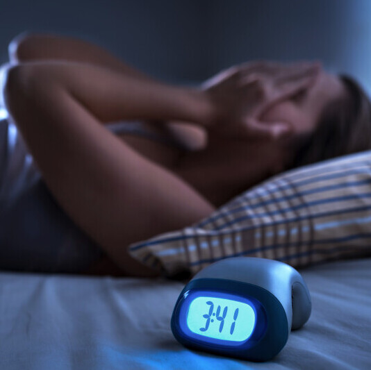A woman in bed with her hands on her face unable to sleep at 3:41am